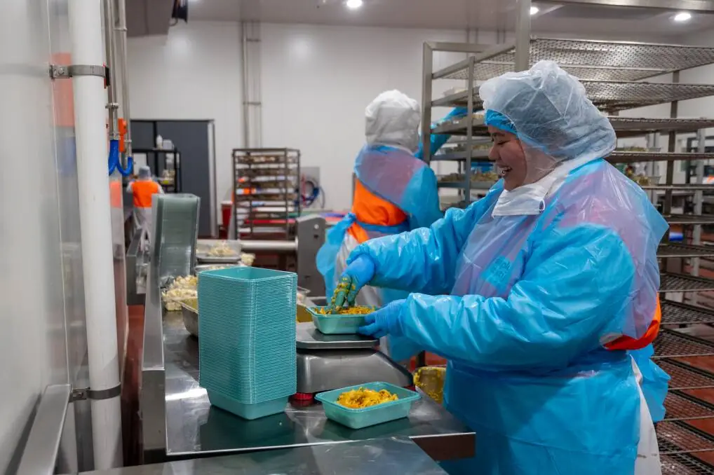 JL King & Co. production team member in blue protective clothing portioning food into trays on a scale